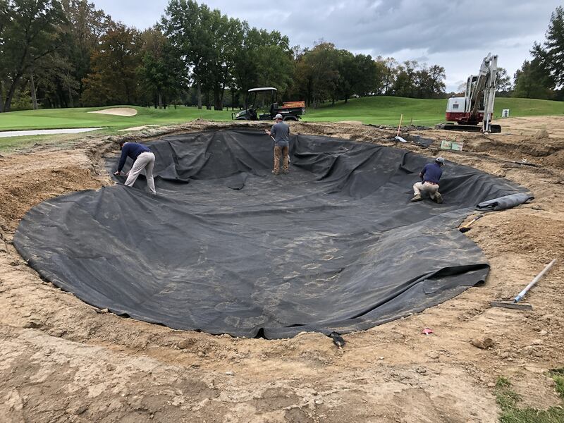 Crew fitting non-woven bunker liner fabric into a large curved golf course bunker
