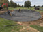 Crew installing black non-woven bunker liner fabric in a golf course sand trap excavation
