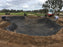 Crew installing bunker liner fabric across a multi-lobed golf course bunker excavation
