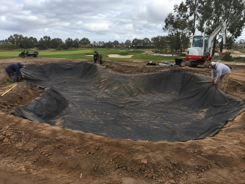 Crew installing bunker liner fabric across a multi-lobed golf course bunker excavation
