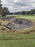 Rolled bunker liner fabric beside a bunker installation near a lakeside green

