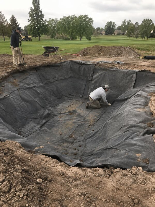 Worker fitting non-woven bunker liner fabric into a bunker with the green and fairway in view
