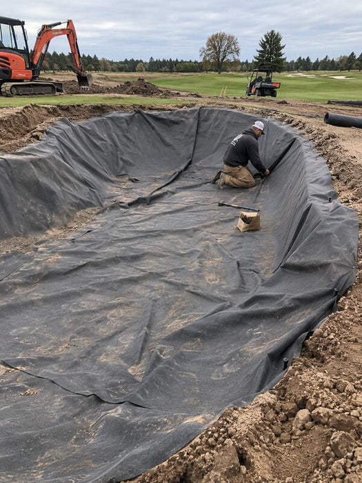Worker securing the edge of non-woven bunker liner fabric along a freshly shaped sand trap
