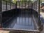 Black HDPE dump trailer liner lining a mesh-sided dump trailer at a jobsite
