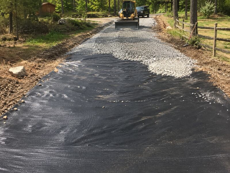 Skid steer grading gravel over gravel driveway fabric
