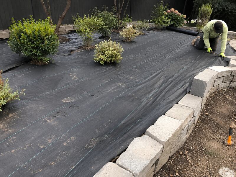 Heavy-duty weed barrier in a large garden bed by a stone wall
