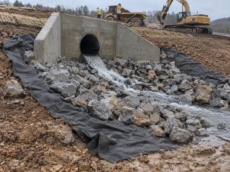 Non-woven geotextile fabric beneath riprap at a hillside culvert outlet with water flowing through
