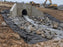 Non-woven geotextile fabric beneath riprap at a hillside culvert outlet with water flowing through
