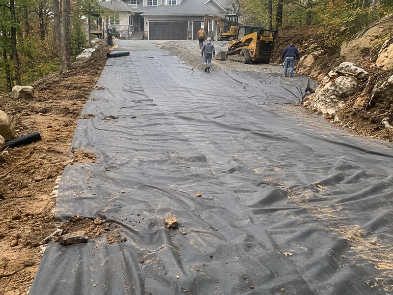 Crew installing non-woven geotextile fabric as a driveway base at a lake house property
