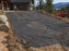 Non-woven geotextile fabric laid as a driveway subbase separator with a mountain lake view in the background

