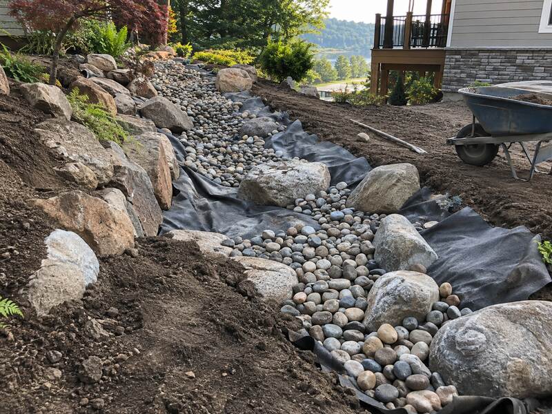 Non-woven geotextile fabric beneath a boulder-lined dry creek bed drainage feature at a lake house
