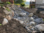 Non-woven geotextile fabric beneath a boulder-lined dry creek bed drainage feature at a lake house
