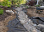 Non-woven geotextile fabric installed beneath a decorative dry creek bed rock drainage feature in a garden
