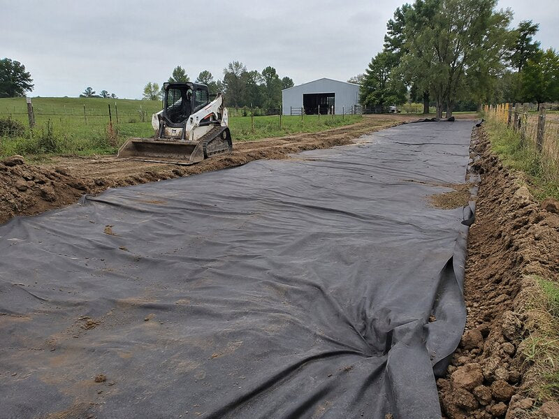Skid steer installing non-woven geotextile fabric as a road base on a farm access road
