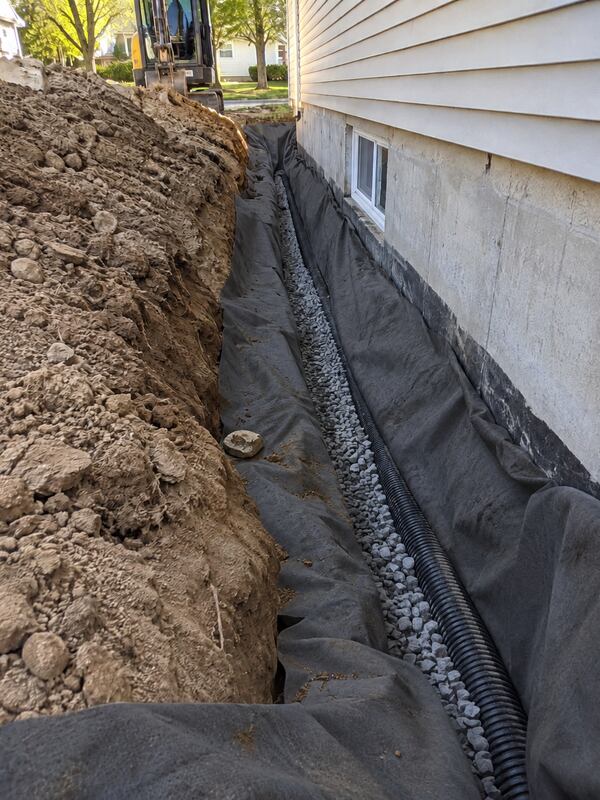 Non-woven geotextile fabric wrapping gravel and pipe in a foundation drain trench along a house
