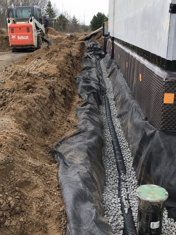 Non-woven geotextile fabric wrapping gravel and drain pipe along a foundation drain system
