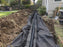 Non-woven geotextile fabric lining a French drain trench beside a backyard patio
