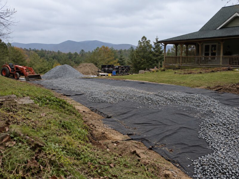 Non-woven geotextile fabric roll laid out under crushed gravel for a rural driveway base
