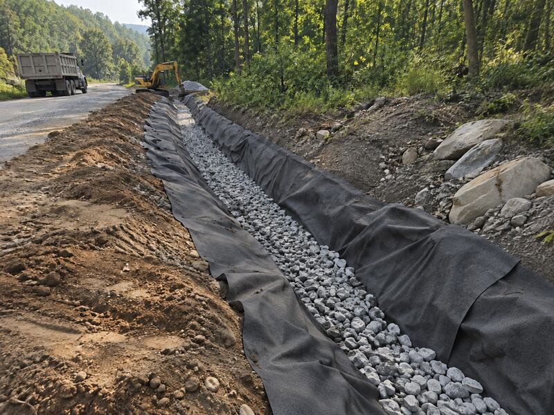 Rock being placed in drainage ditch along roadside