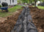 Non-woven geotextile fabric lining a French drain trench filled with gravel in a backyard

