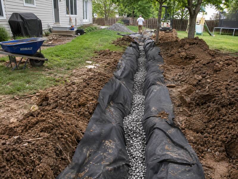 Non-woven geotextile fabric lining a French drain trench filled with gravel in a backyard
