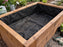 Non-woven planter box liner fabric installed inside a raised garden bed with potted seedlings nearby
