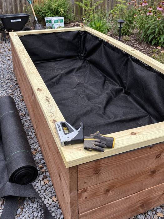 Rolled planter box liner fabric and staple gun beside a lined raised garden bed
