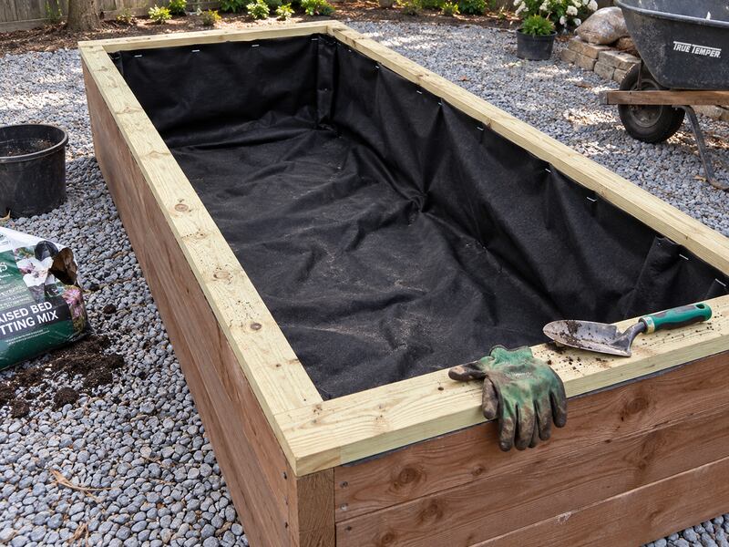 Non-woven raised bed liner fabric fitted inside a wood planter box on a gravel patio

