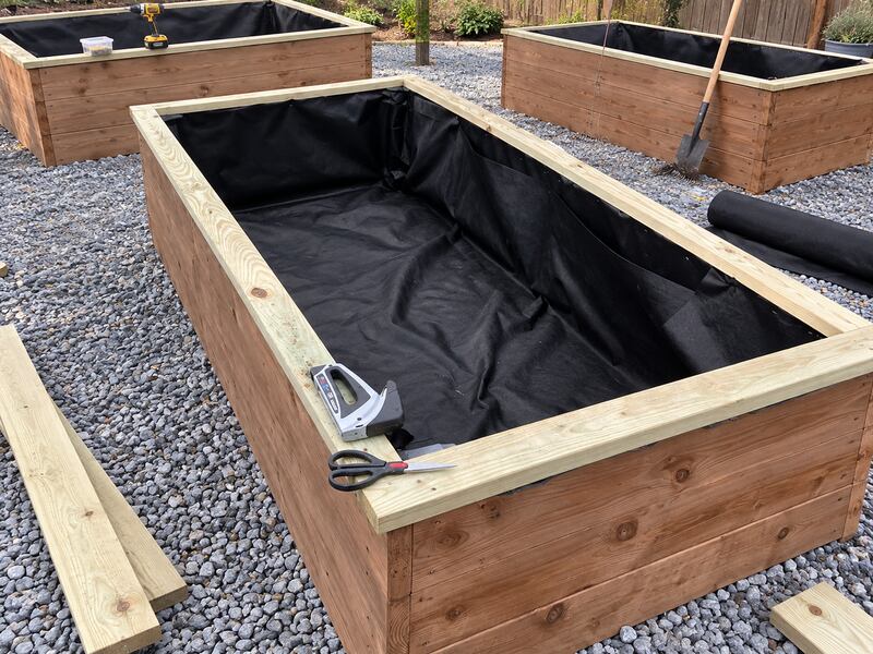 Non-woven raised bed liner fabric installed across multiple wood planter boxes in a garden layout
