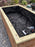 Staple gun and scissors resting on raised bed liner fabric inside a wood planter box

