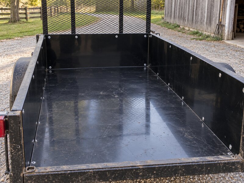 Black HDPE trailer liner installed inside a mesh-sided utility landscape trailer
