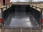 Black HDPE trailer liner in a mesh-sided utility trailer parked near a farm barn and hay bales
