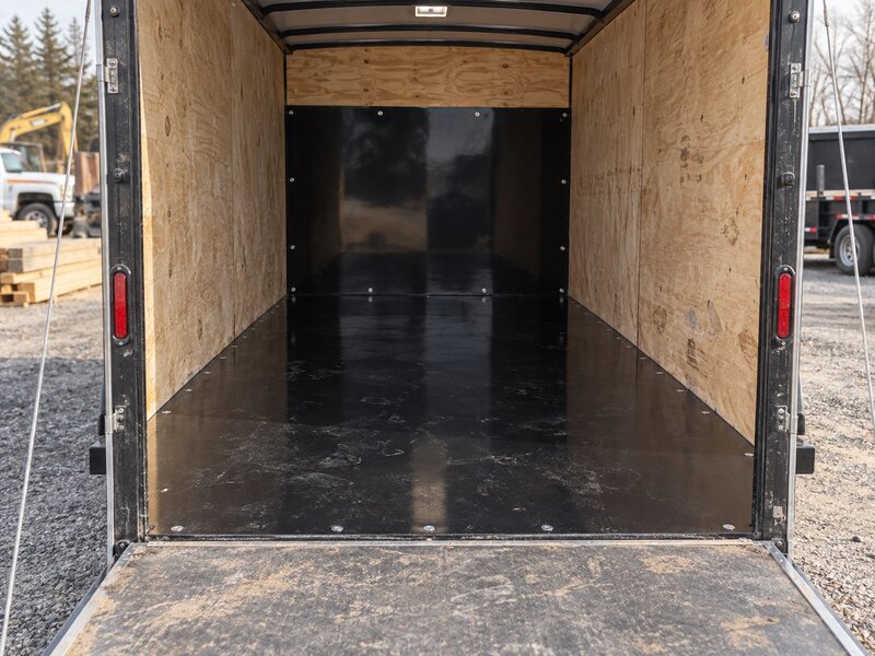 Black HDPE trailer liner lining an open utility trailer bed parked at a farm shop
