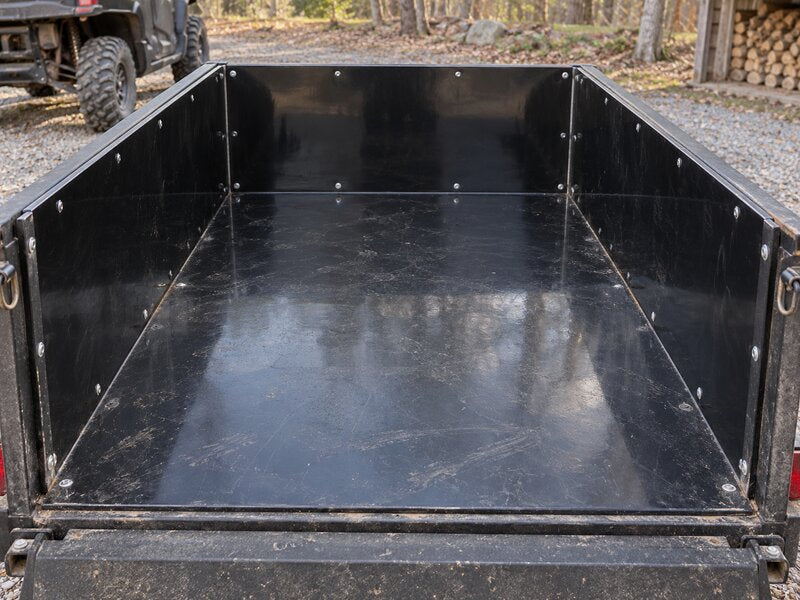 Black HDPE trailer liner lining a utility trailer bed on a wooded gravel driveway
