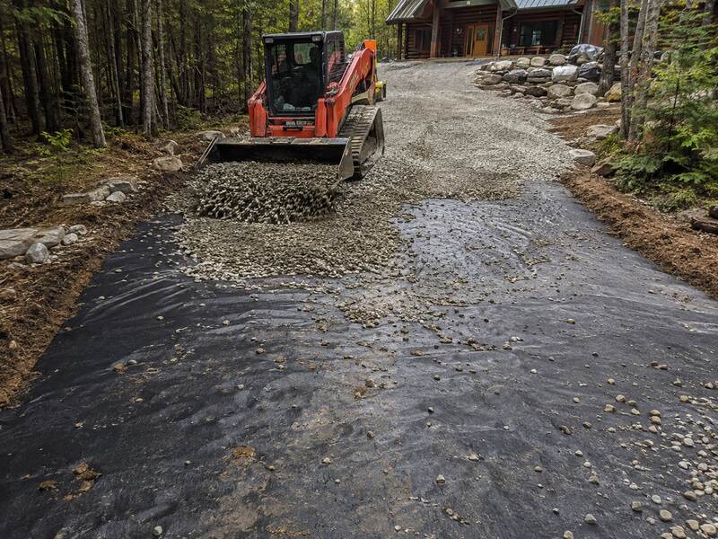 Skid steer placing gravel over woven geotextile fabric for driveway base stabilization
