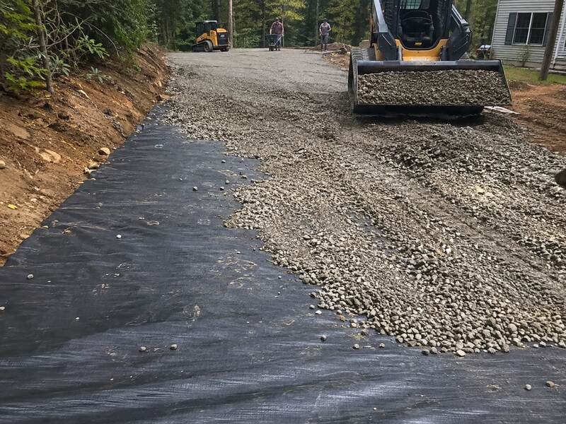 Skid steer spreading gravel over woven geotextile fabric on a driveway
