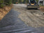 Skid steer spreading gravel over woven geotextile fabric on a driveway
