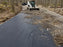 Skid steer spreading gravel over woven geotextile fabric on a driveway

