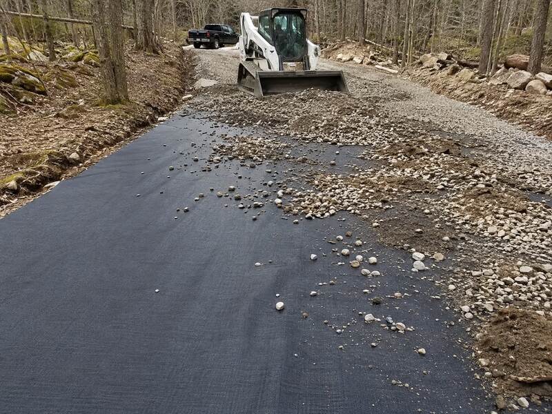 Skid steer spreading gravel over woven geotextile fabric on a driveway
