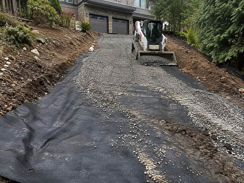 Skid steer spreading gravel over woven geotextile fabric on a sloped driveway
